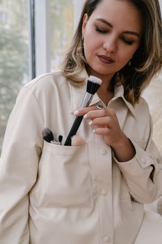 A young woman in a white shirt holding a makeup brush from her pocket.