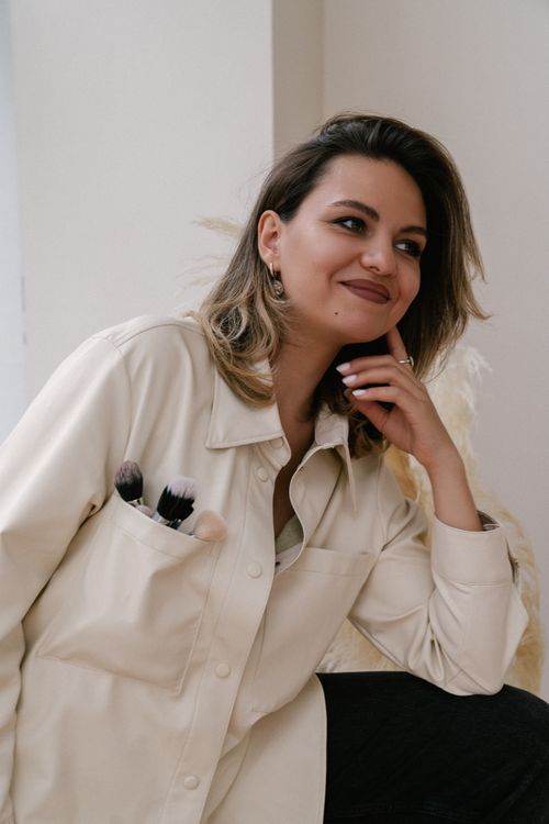 Free Young woman with makeup brushes in a pocket, smiling indoors in a white shirt. Stock Photo