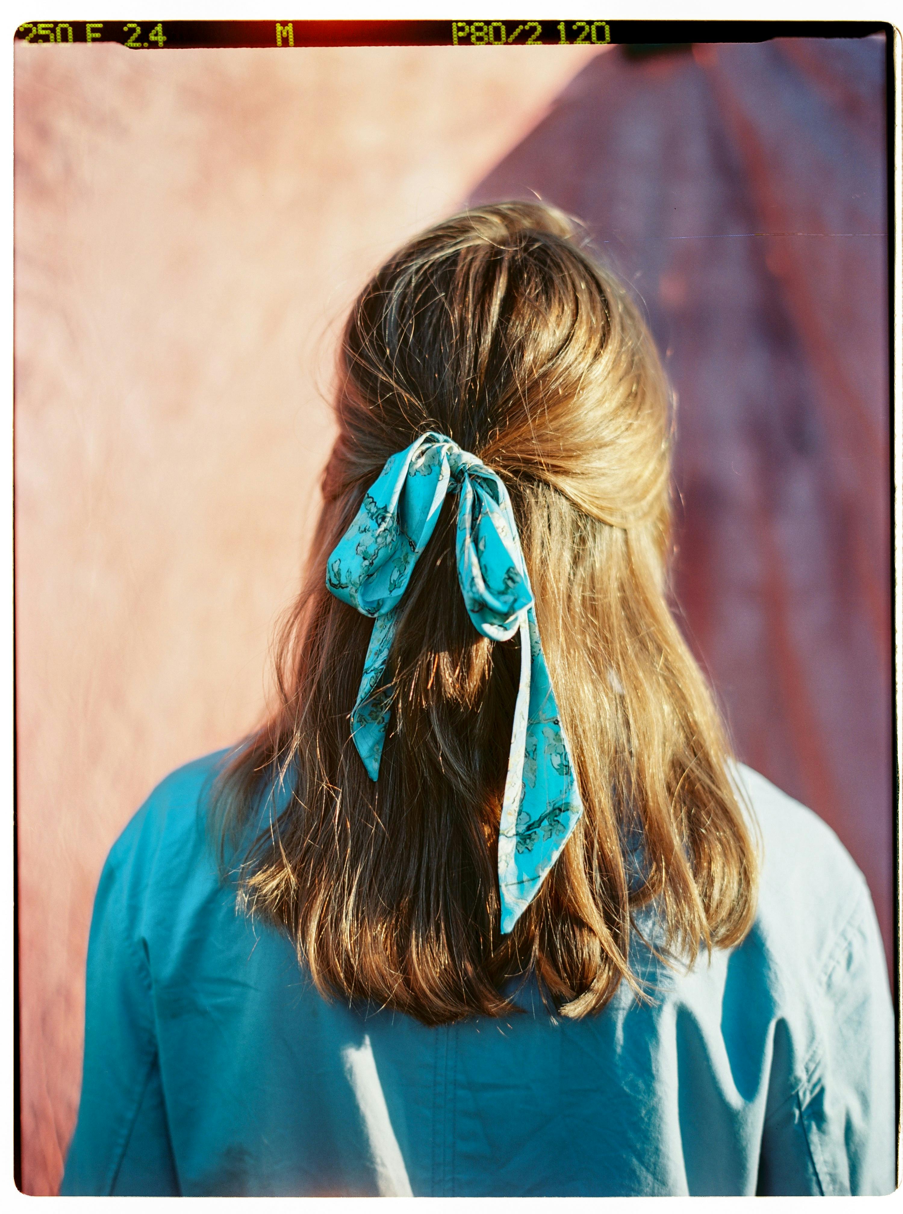 Rear view portrait of a woman with brown hair tied with a blue scarf.