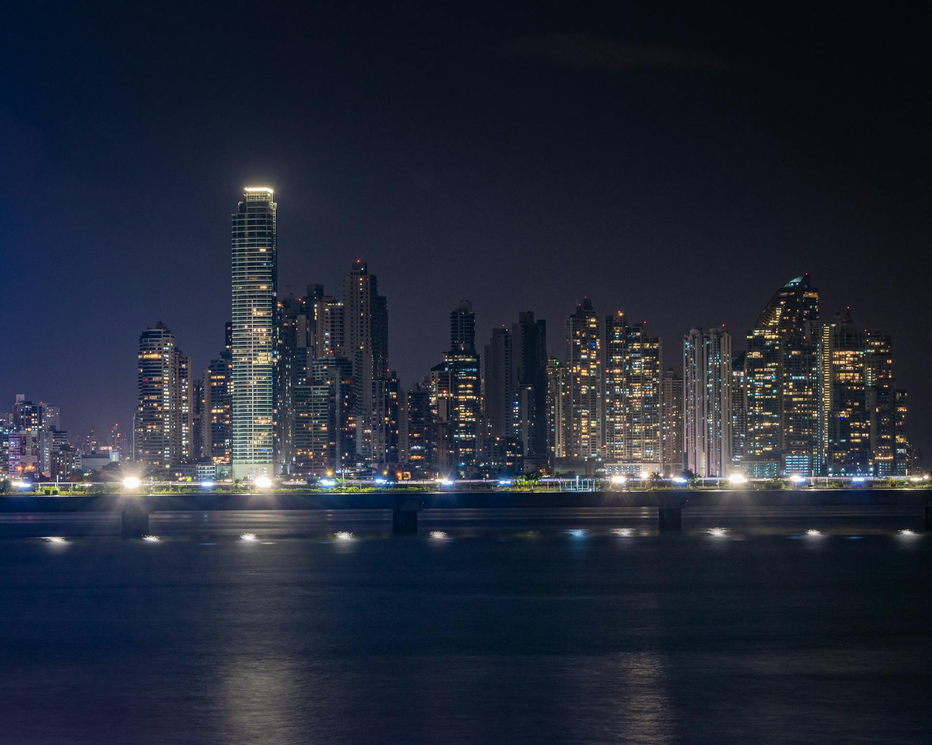 Dramatic night view of Panama City skyline with illuminated skyscrapers reflected on the water.