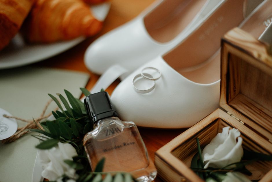 Imagem de itens de casamento, incluindo saltos brancos, alianças, buquê e perfume, simbolizando o planejamento e celebração do casamento.