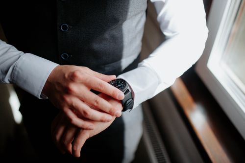 Free Close-up of a man adjusting his wristwatch, dressed elegantly in a vest and shirt, near a window. Stock Photo