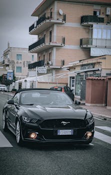 A sleek black convertible sports car driving on a city street with urban background.