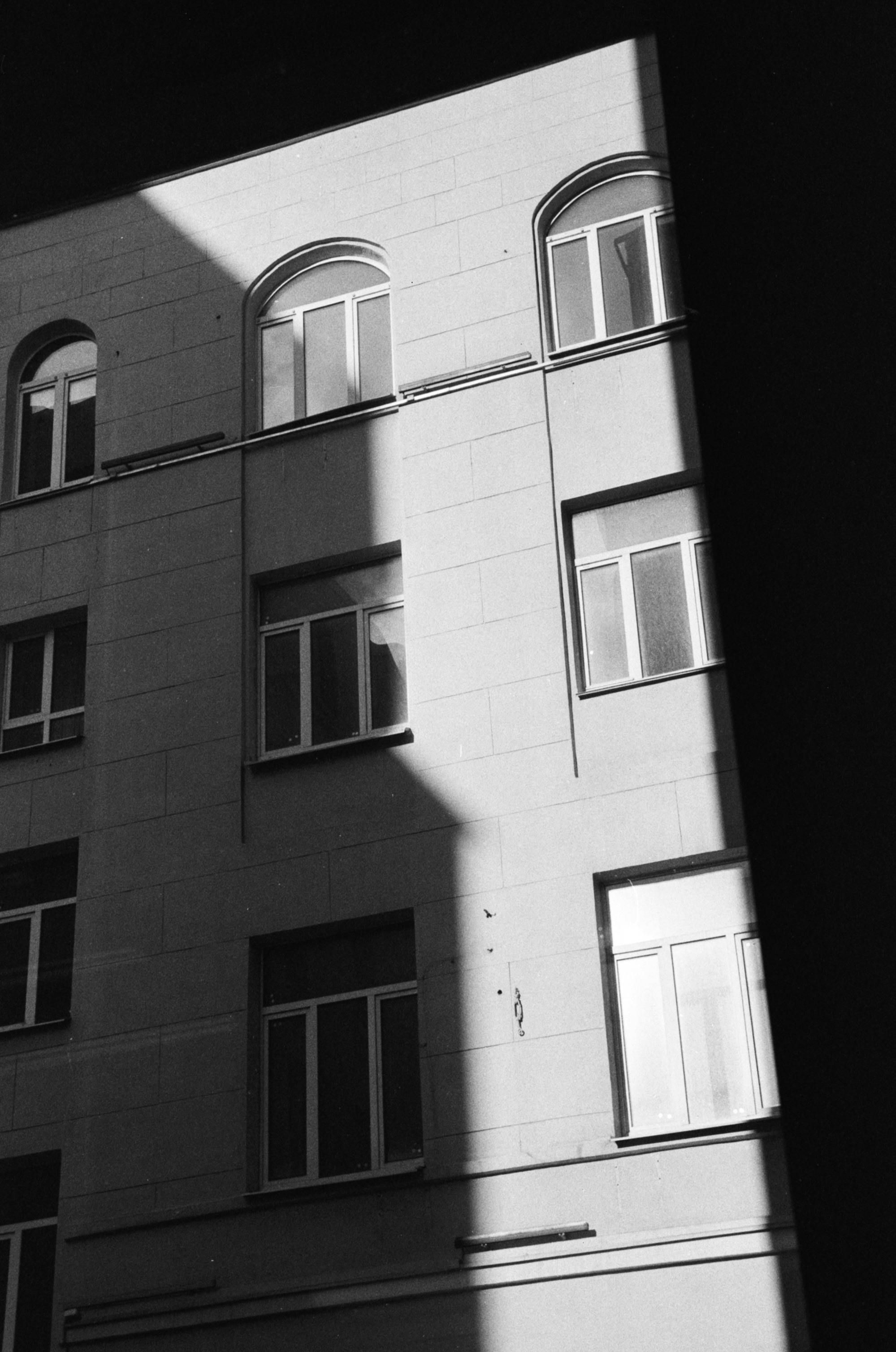 Black and white photo of a building facade in Moscow, showcasing shadows and windows.