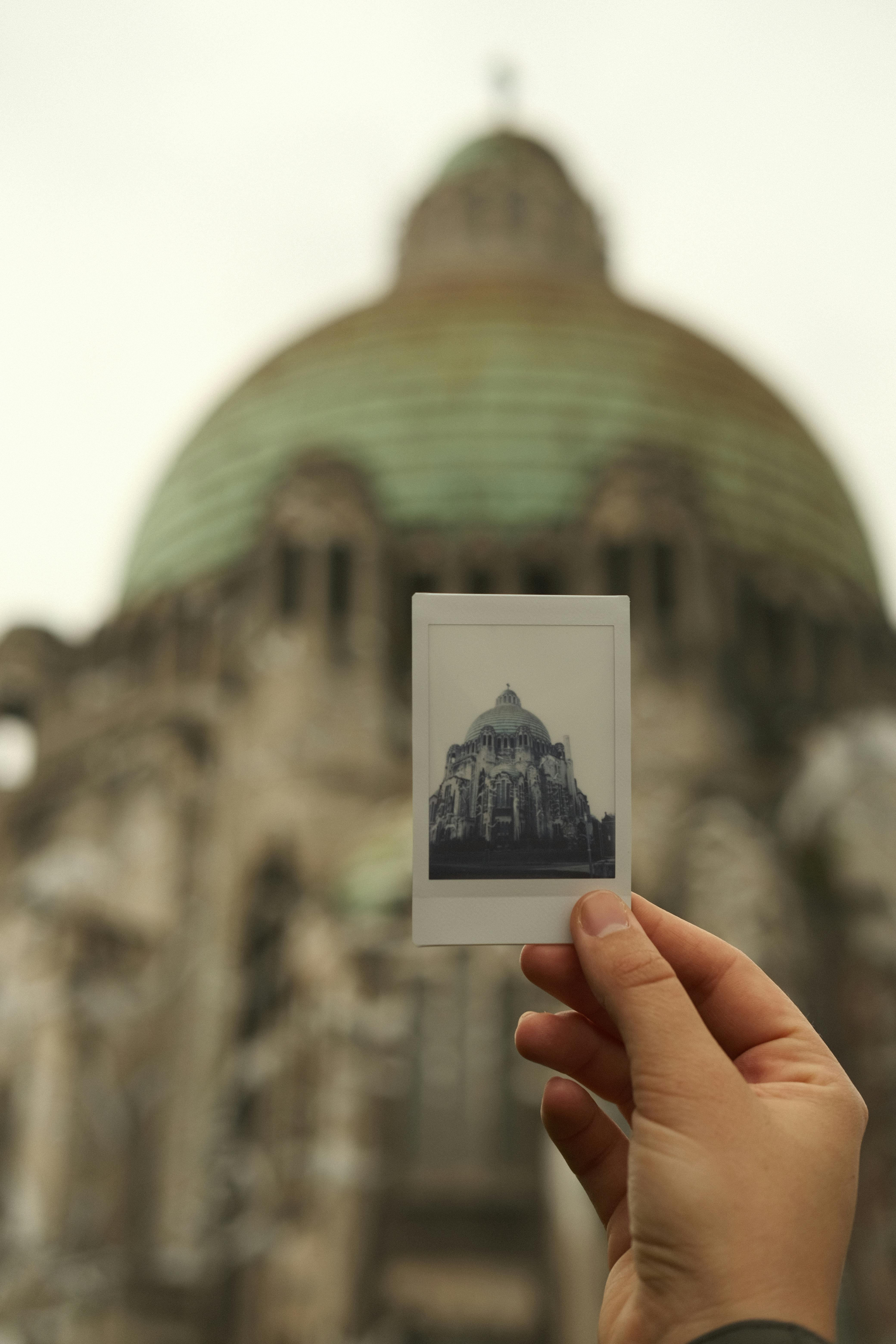 A hand holds a Polaroid of a famous church in Liège, Belgium, showcasing its architecture.
