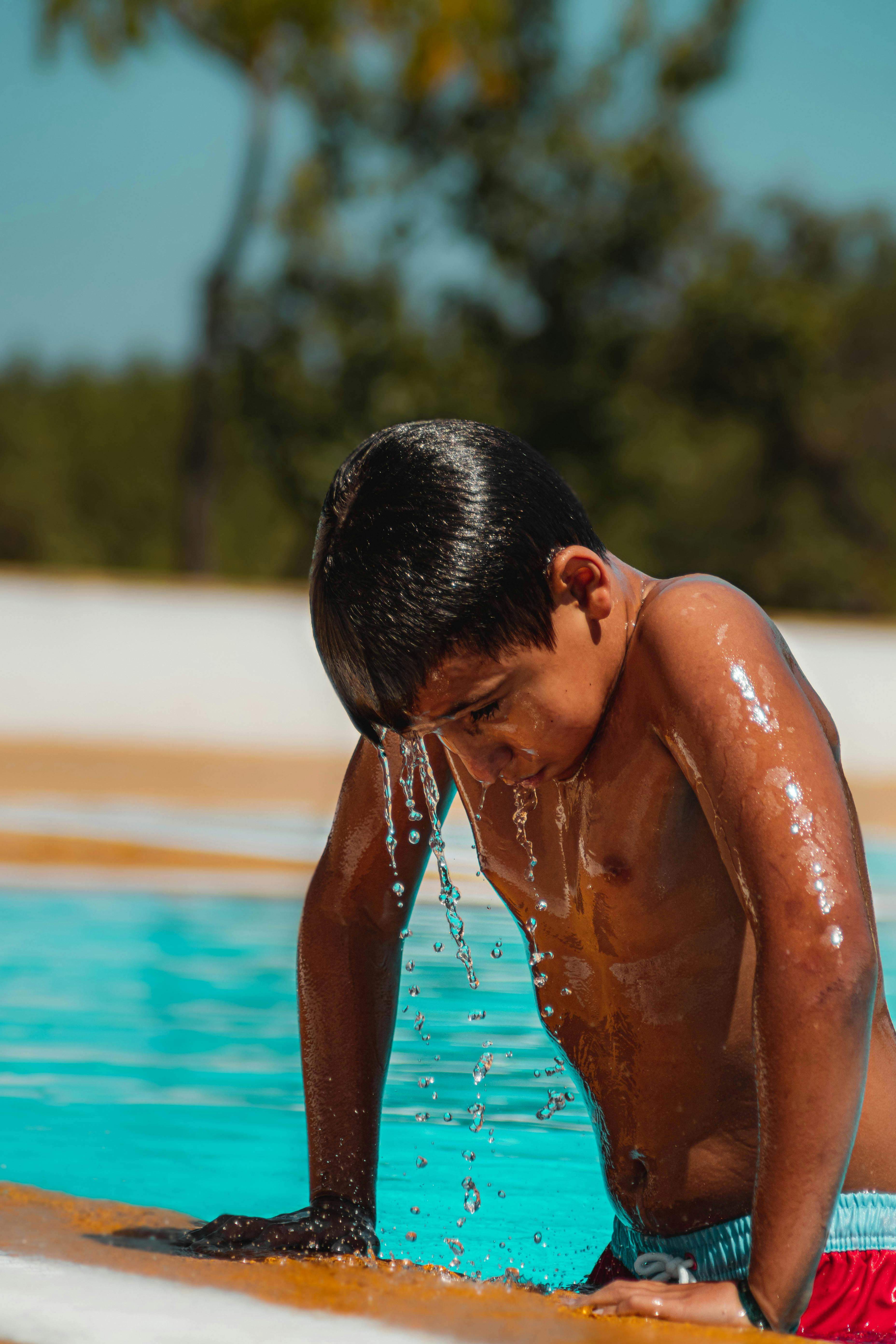 a shirtless boy coming out of the swimming pool with dripping water