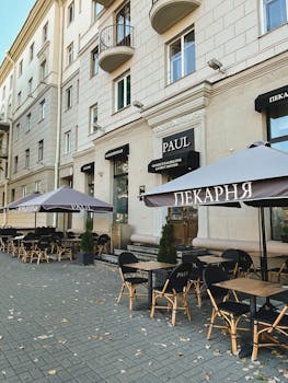 Outdoor street cafe with tables, chairs, and umbrellas on a city sidewalk.