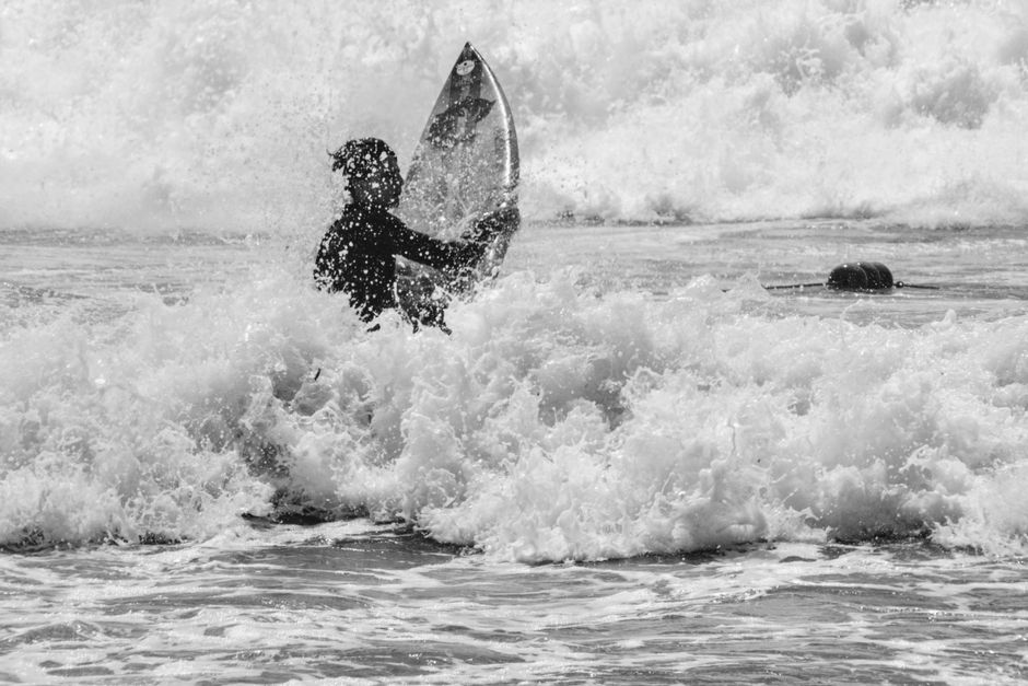 A surfer skillfully navigates crashing waves in a monochromatic scene.