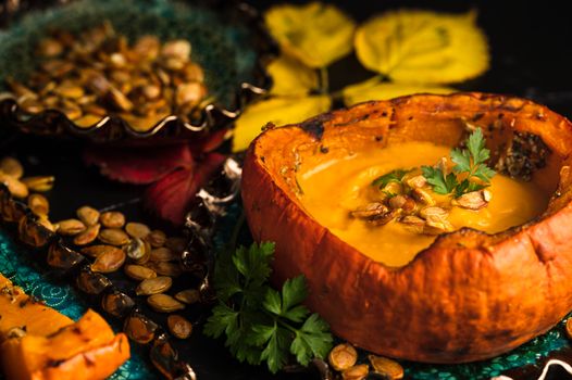 Delicious pumpkin soup served in a pumpkin with seeds and autumn leaves.