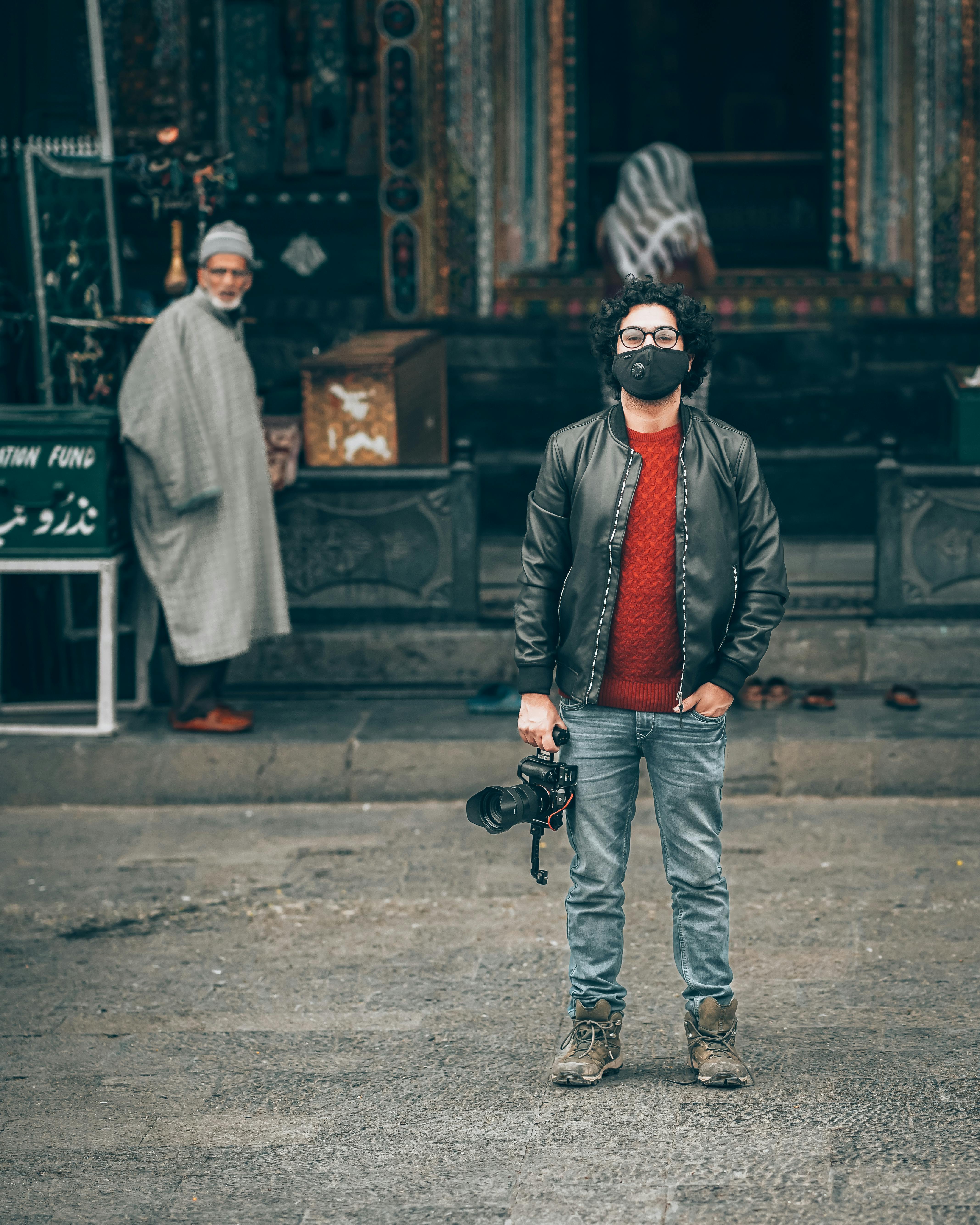 a man in black jacket and blue denim jeans holding a black dslr camera