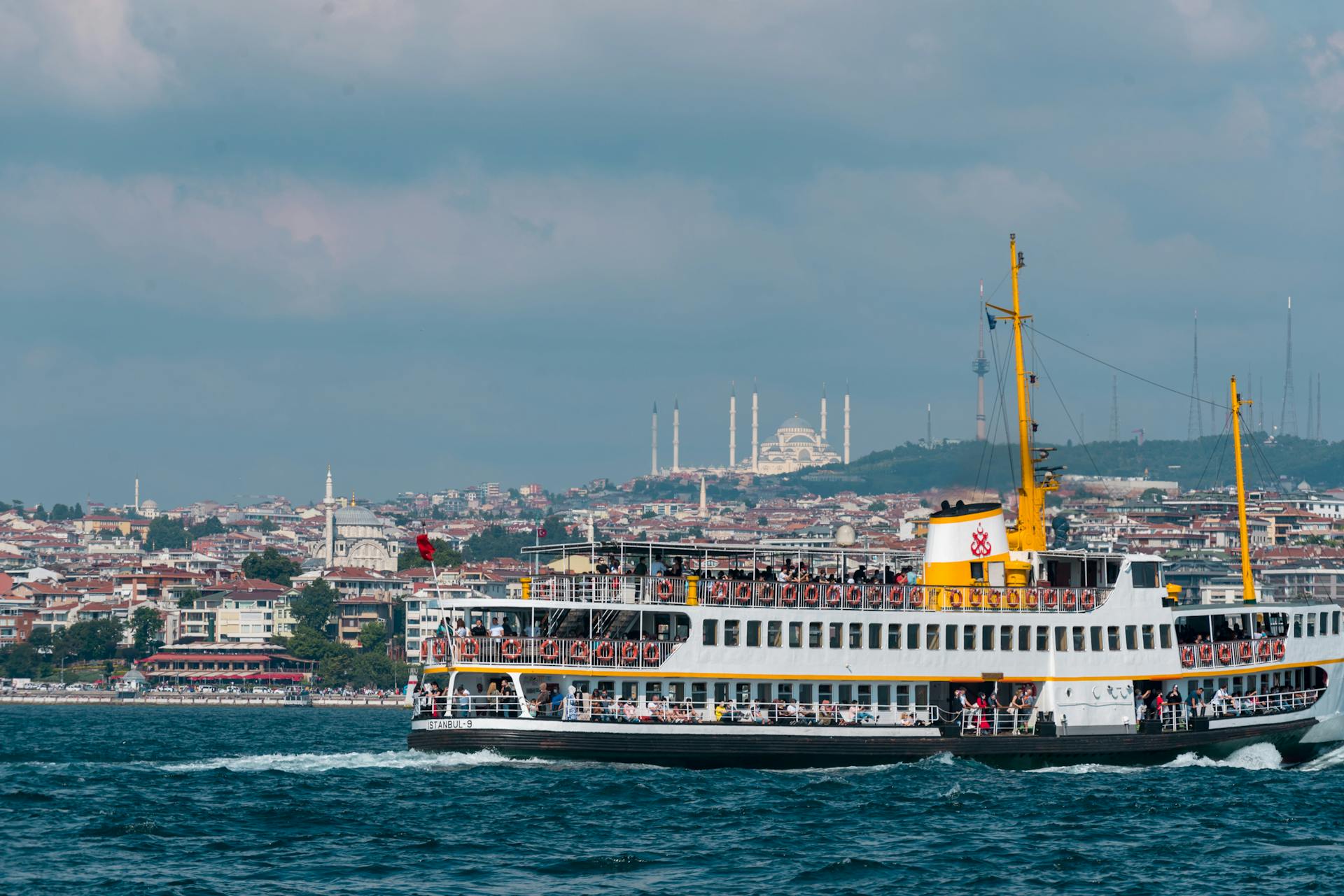 A ferry boat traverses the Bosphorus with a city skyline in the background, showcasing vibrant maritime activity.
