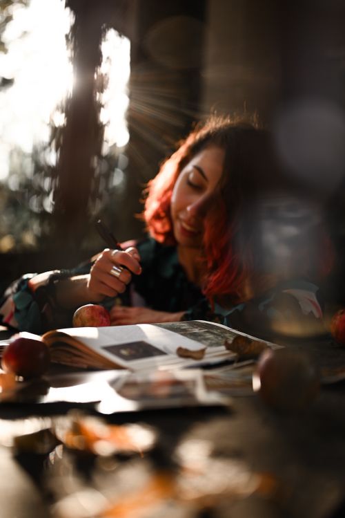 Free Woman reading in warm sunlight surrounded by apples, capturing a cozy, serene atmosphere. Stock Photo