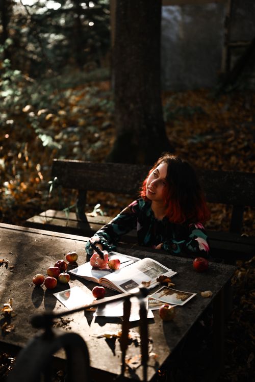 Free A woman enjoys a peaceful moment at an outdoor table in autumn, surrounded by apples and nature. Stock Photo