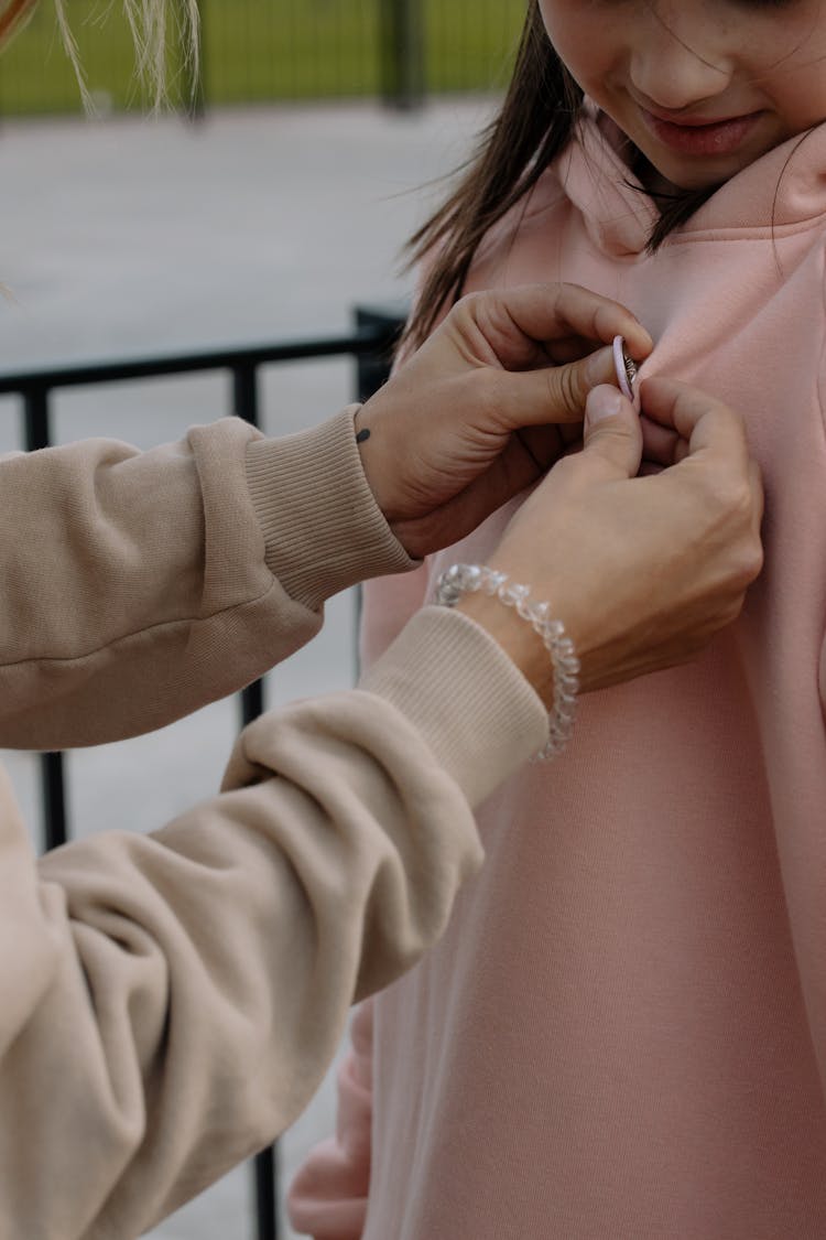 A Person Putting A Pin On A Young Girl's Jacket