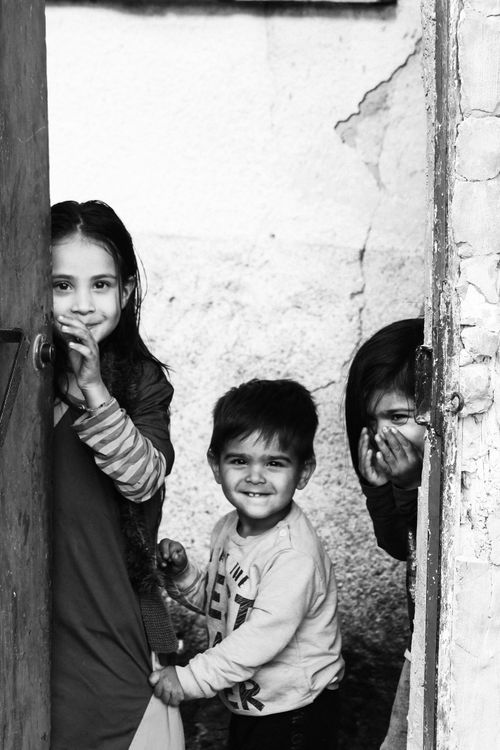 Free Grayscale image of three smiling children peeking from a door. Stock Photo