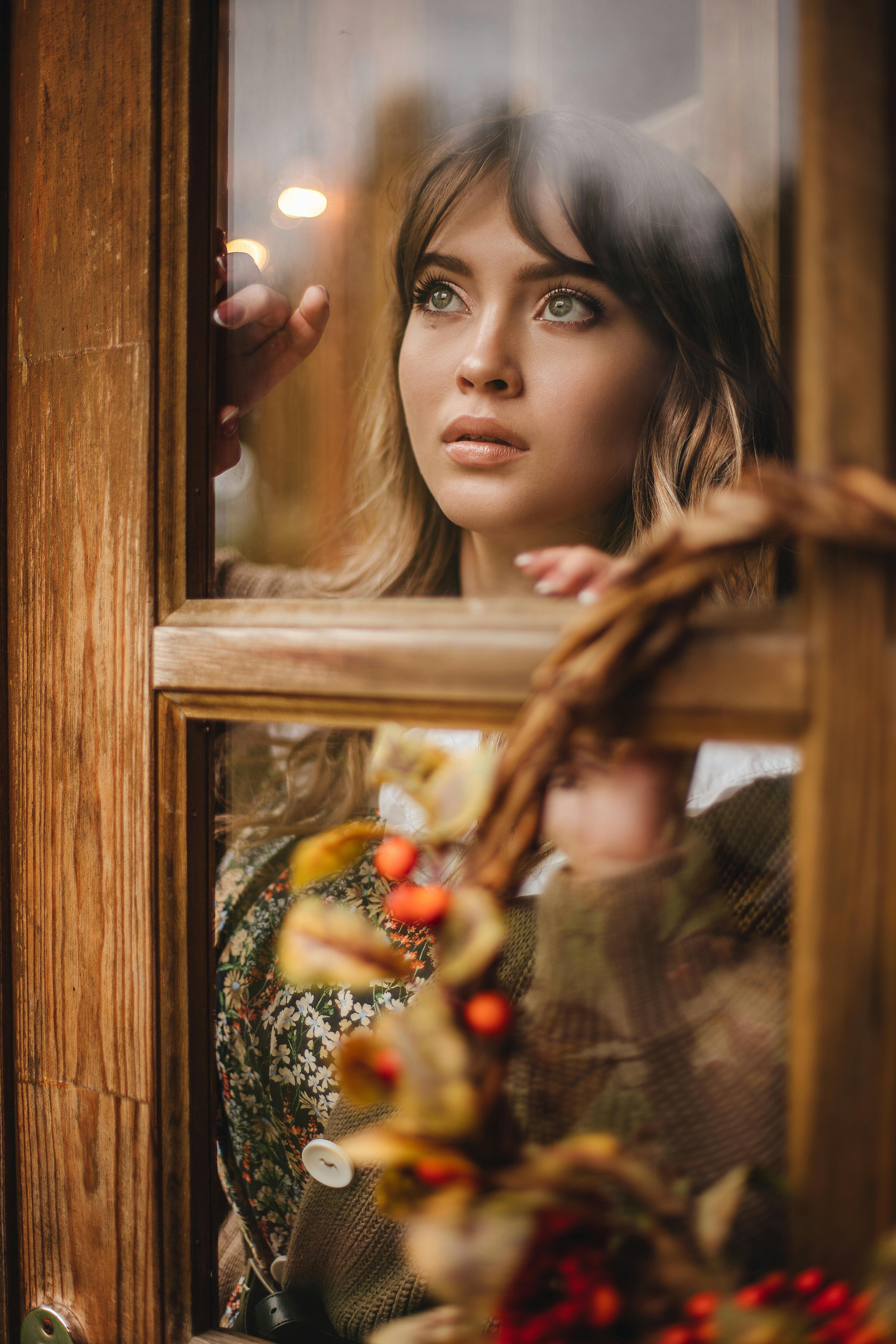 Portrait of a woman with long brown hair looking through a window adorned with autumn decor.