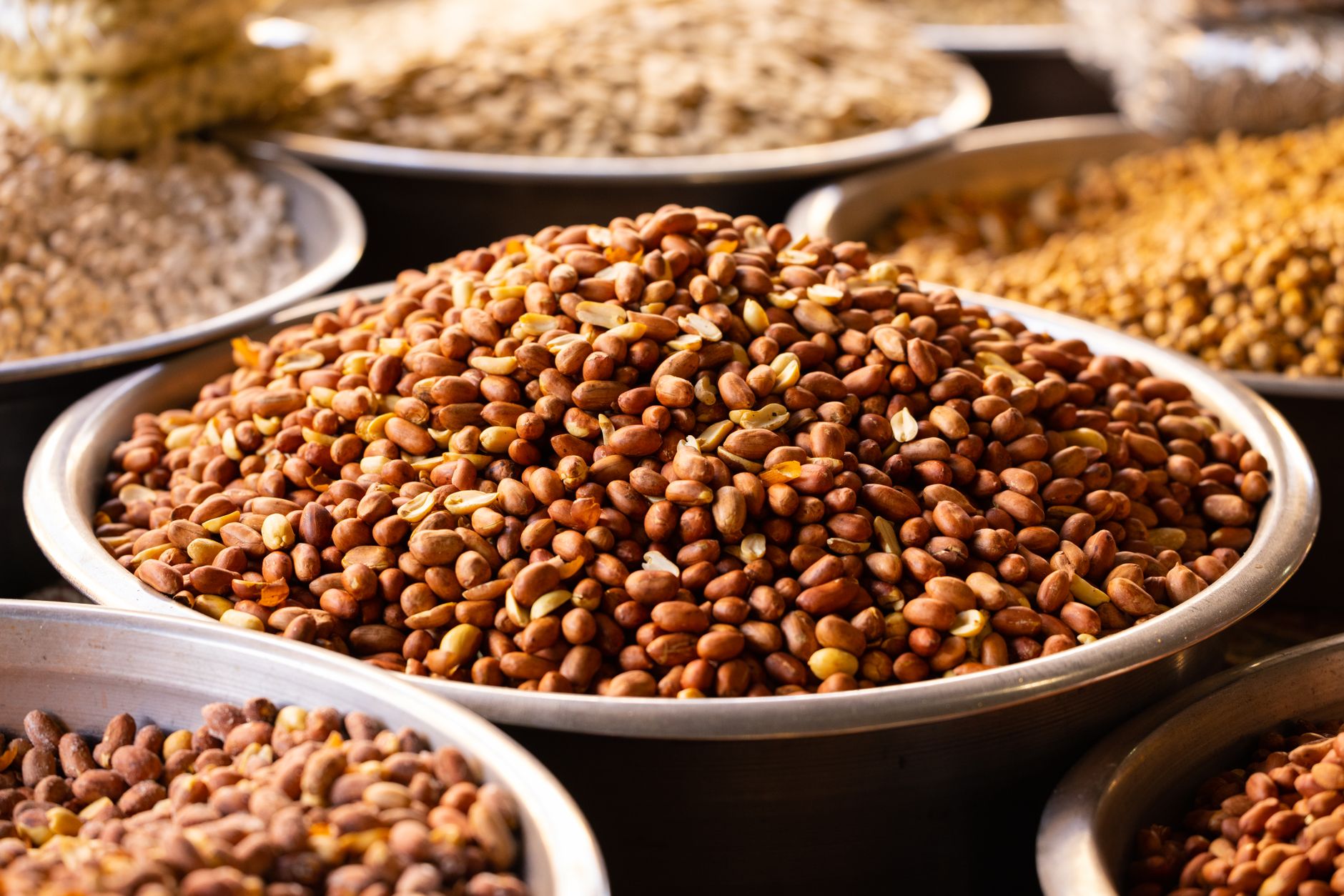 Close-up of roasted nuts in stainless bowls at a market, showcasing a variety of healthy and nutritious snacks.