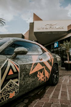 Close-up of a sports car with a unique camouflage design in front of a modern gym.