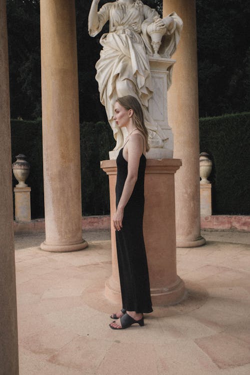 Woman in Black Sleeveless Dress Standing Beside a Statue