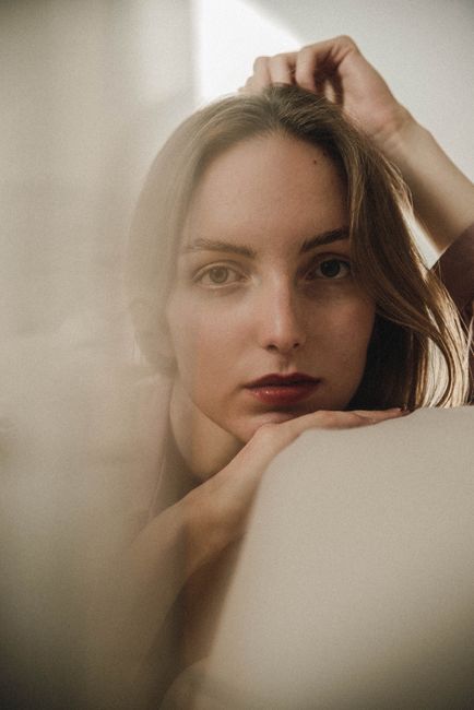 Intimate portrait of a young woman resting her head on her arms with a soft, dreamy expression.