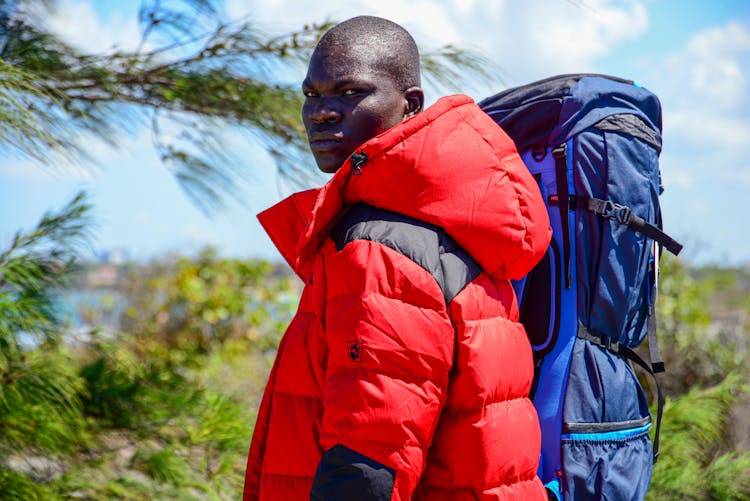 A Man In Red Jacket Carrying His Backpack While Looking Over Shoulder