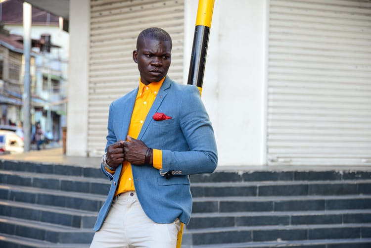 A Man Leaning On The Black And Yellow Pole On The Street