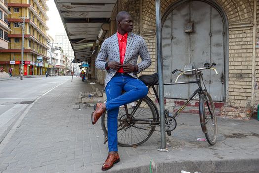 A Man in Denim Jeans and Printed Suit Sitting on the Street while Looking Over Shoulder