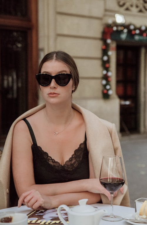 A Woman Wearing Sunglasses Sitting at the Table with Red Wine