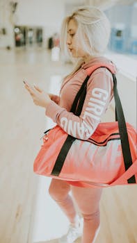 Young woman in sportswear using phone, holding pink duffle bag