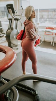 Blonde woman in pink sportswear standing indoors in gym, showcasing fit physique. Bright and dynamic.
