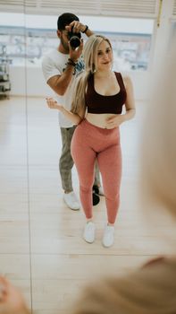 Man and woman taking a mirror selfie in activewear. Bright indoor gym setting.