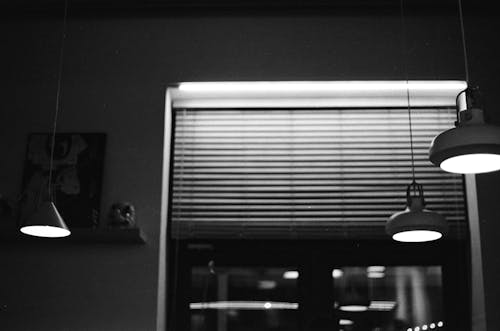 Grayscale Photo of Window Blinds and Pendant Lamps