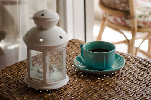 Lanterna A Candela Bianca Accanto Alla Tazza Da Caffè In Ceramica Blu Sul Tavolo Di Vimini