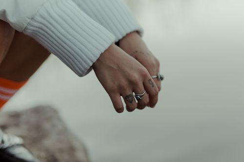 Free A close-up of tattooed hands adorned with rings against a calm lakeside background. Perfect for lifestyle and nature themes. Stock Photo