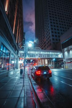 A vibrant city street in Minneapolis featuring high-rise buildings and reflections on wet pavement at night.