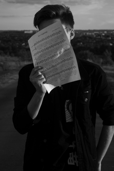 Monochrome image of a person holding sheet music covering face.