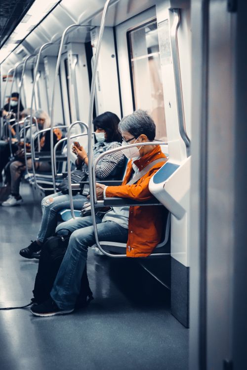 Free Commuters wearing face masks sit inside a contemporary subway train during travel. Stock Photo