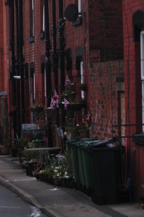 Free Narrow alley with red brick buildings adorned with British flags and green trash cans. Stock Photo