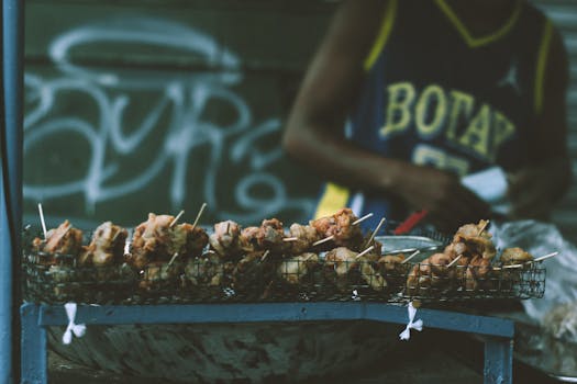 Street vendor preparing grilled skewers at an outdoor food stall with graffiti backdrop.