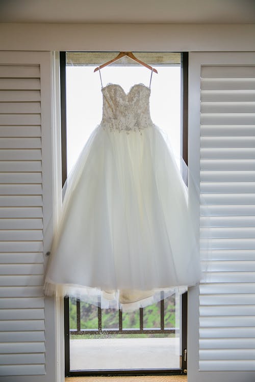 A White Wedding Gown Hanging on Glass Window