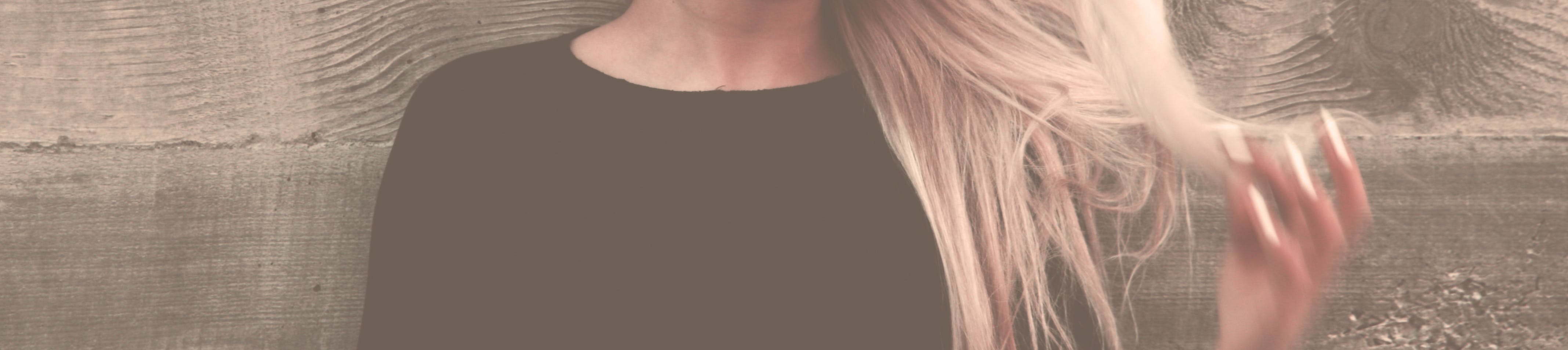 Close-up portrait of a woman with long, flowing blonde hair against a textured background.