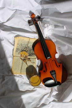 Artistic arrangement with a violin, coffee, and book on white cloth.