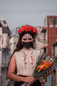 Woman in traditional Day of the Dead costume with floral patterns and mask outdoors.
