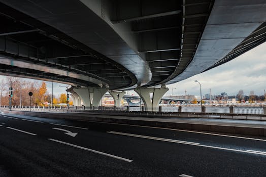 Wide view of modern bridge structure with cityscape background under a cloudy sky.