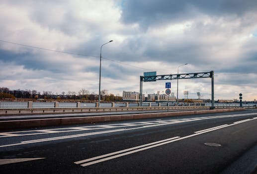 A deserted road stretches towards the horizon, displaying overcast skies and distant city building.