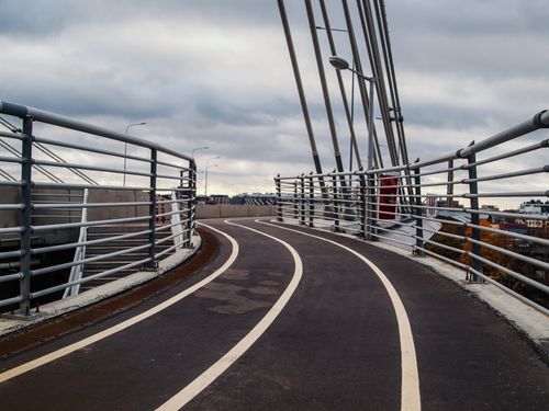 Free Curved bicycle lane on a modern bridge with metal railings and cloudy skies. Stock Photo