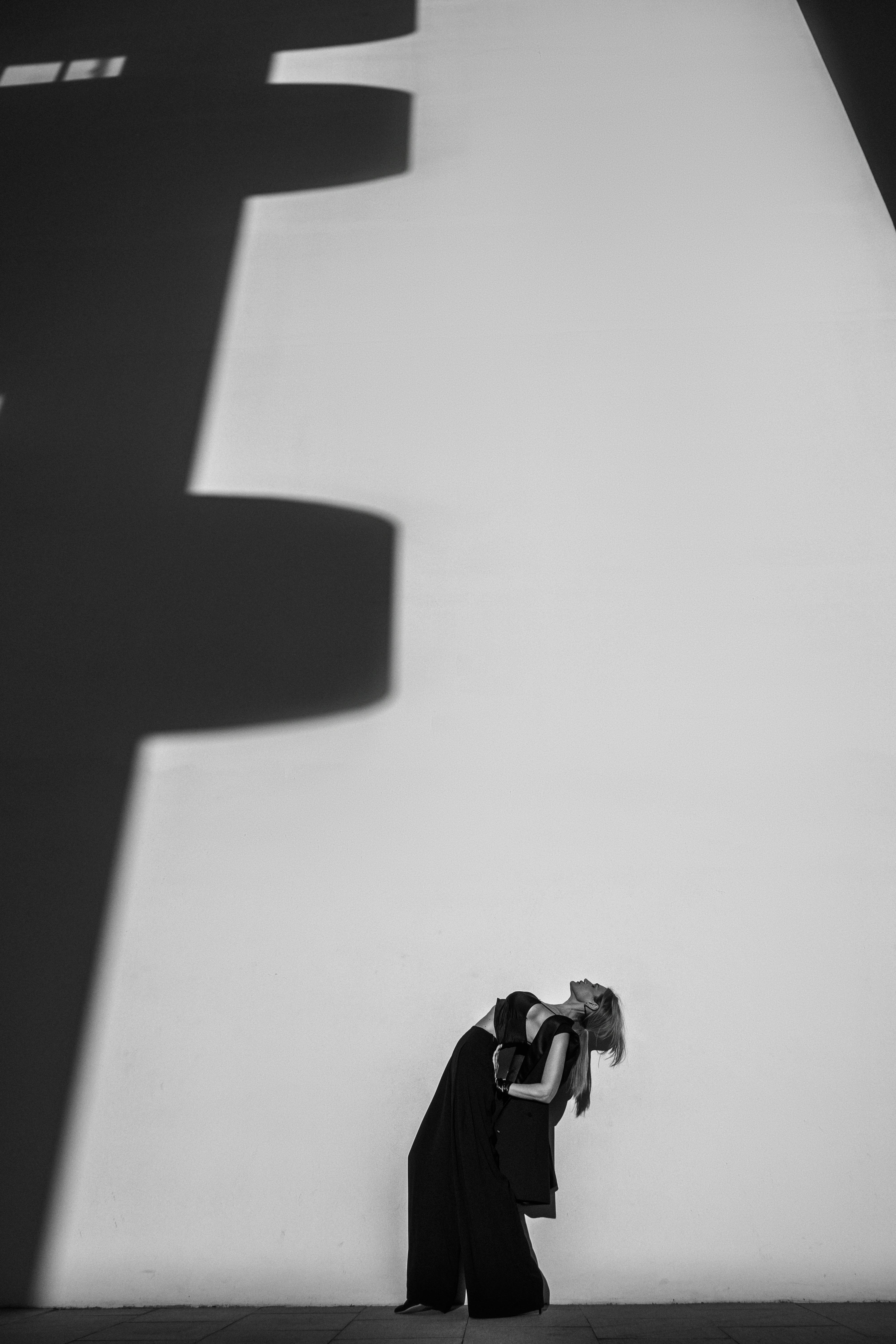 Minimalist black and white photo with shadows, featuring a woman posing creatively.