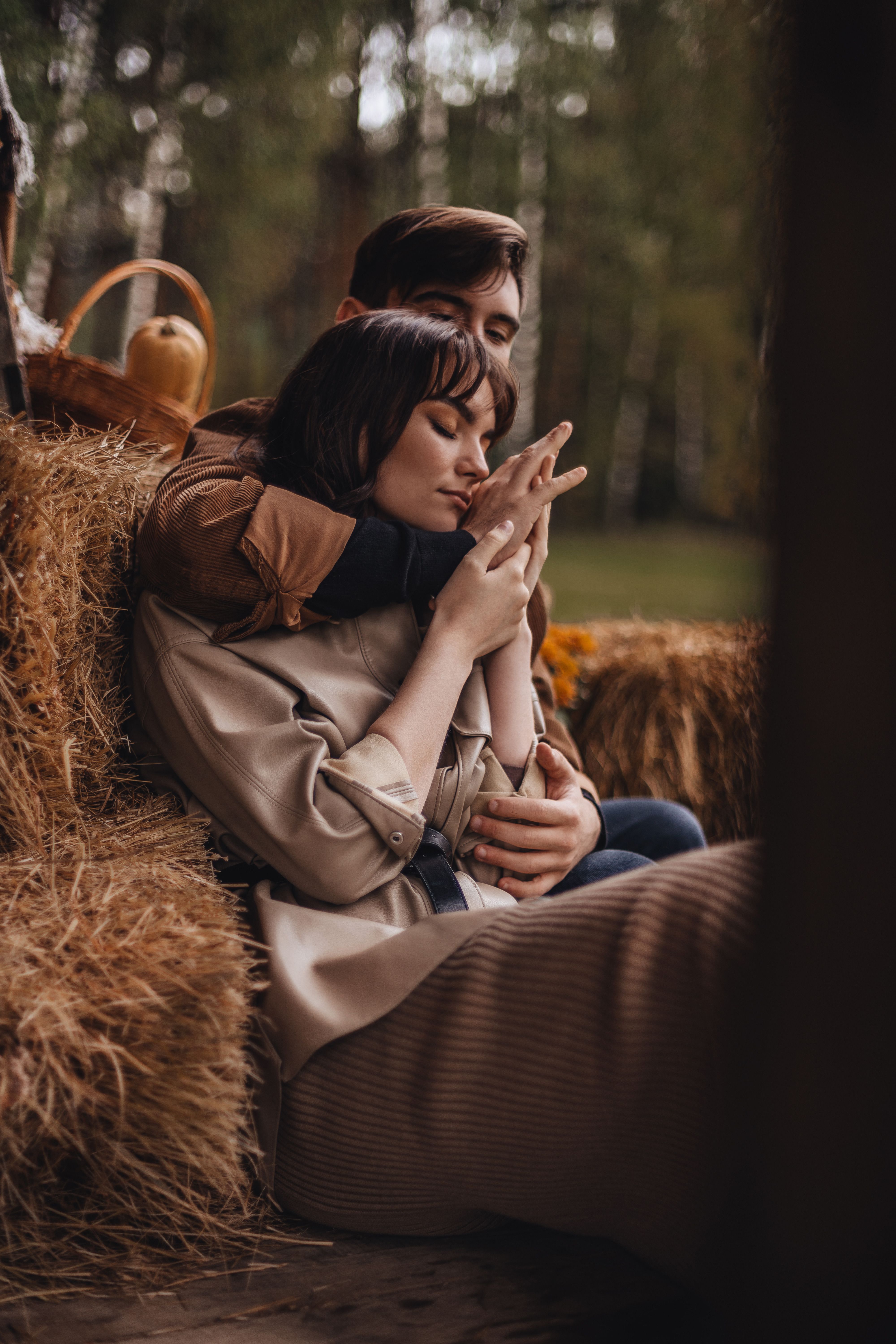 A couple sitting on hay bales in an embrace, enjoying a rustic outdoor scene.