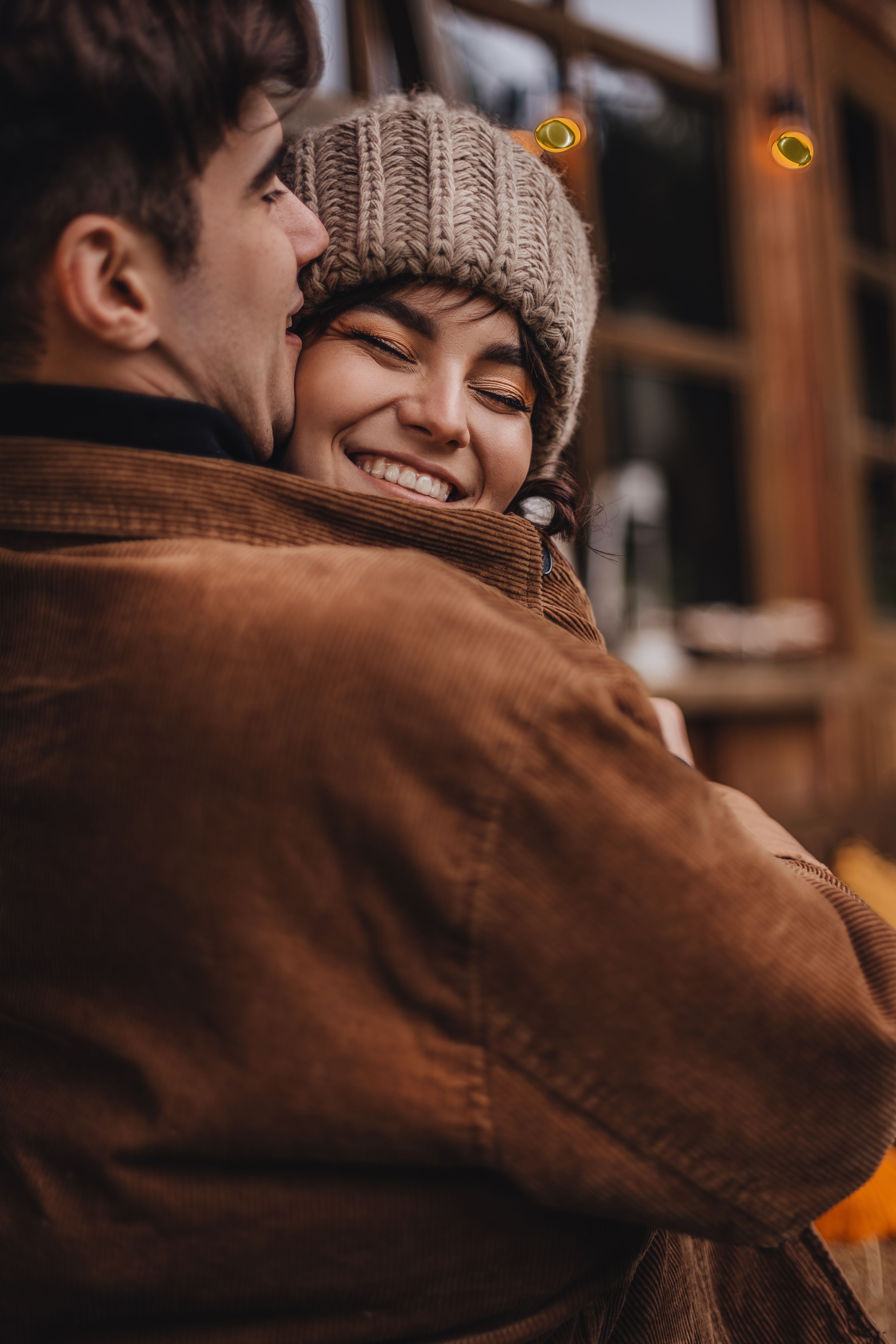 A warm embrace shared by a smiling couple in cozy winter attire outdoors.