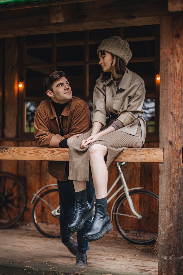 Woman Sitting On Railing And Man Standing Beside Her